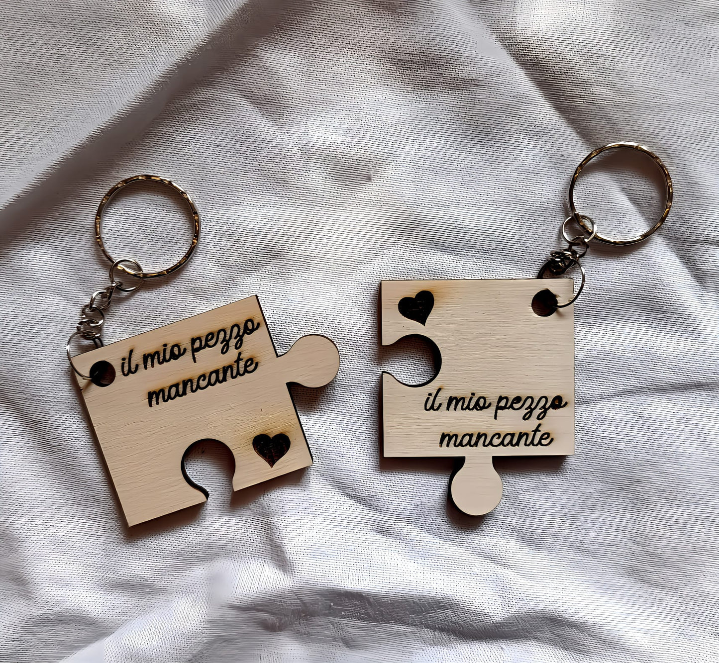 Wooden puzzle piece keychains with 'il mio pezzo mancante' on white fabric background