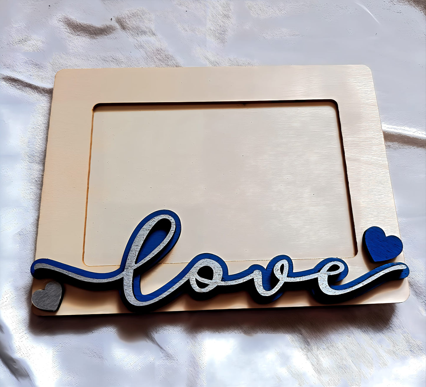 Wooden photo frame with blue and silver 'love' text and heart shapes on white fabric