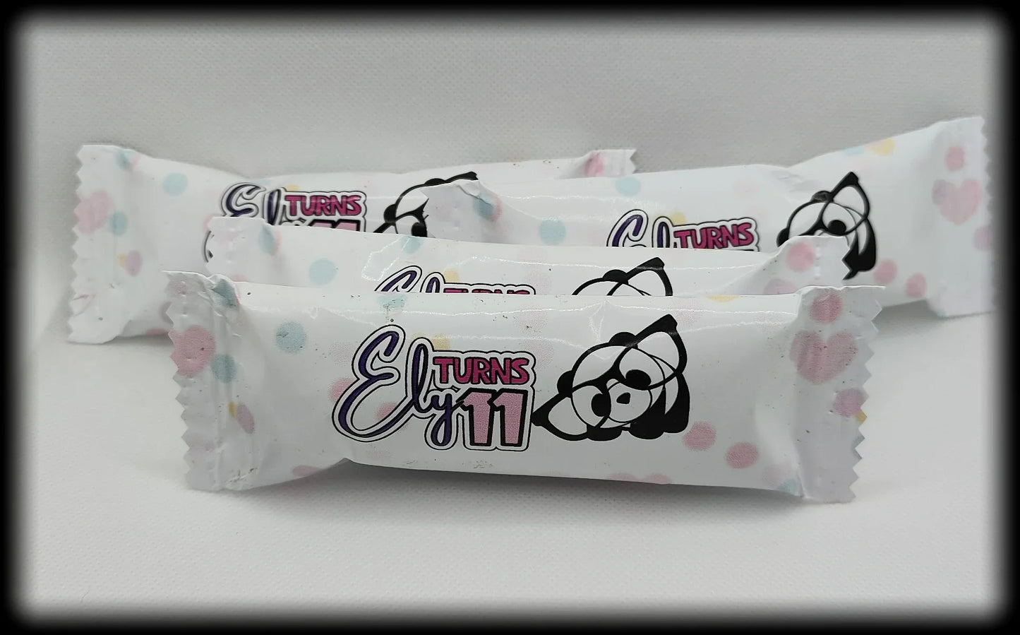 Birthday candy wrappers with 'Ely Turns 11' and cartoon raccoon, pastel polka dot design