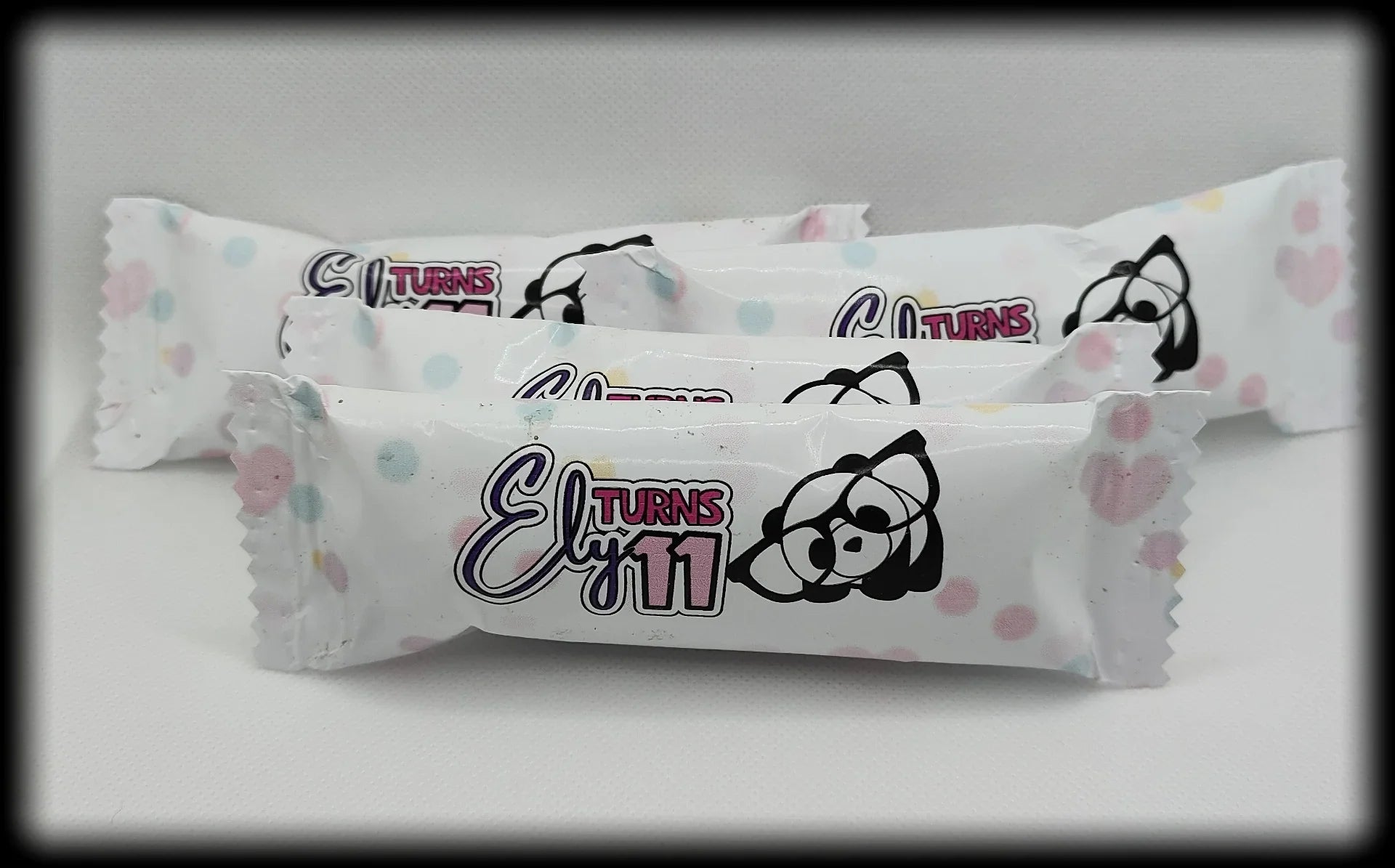 Birthday candy wrappers with 'Ely Turns 11' and cartoon raccoon, pastel polka dot design