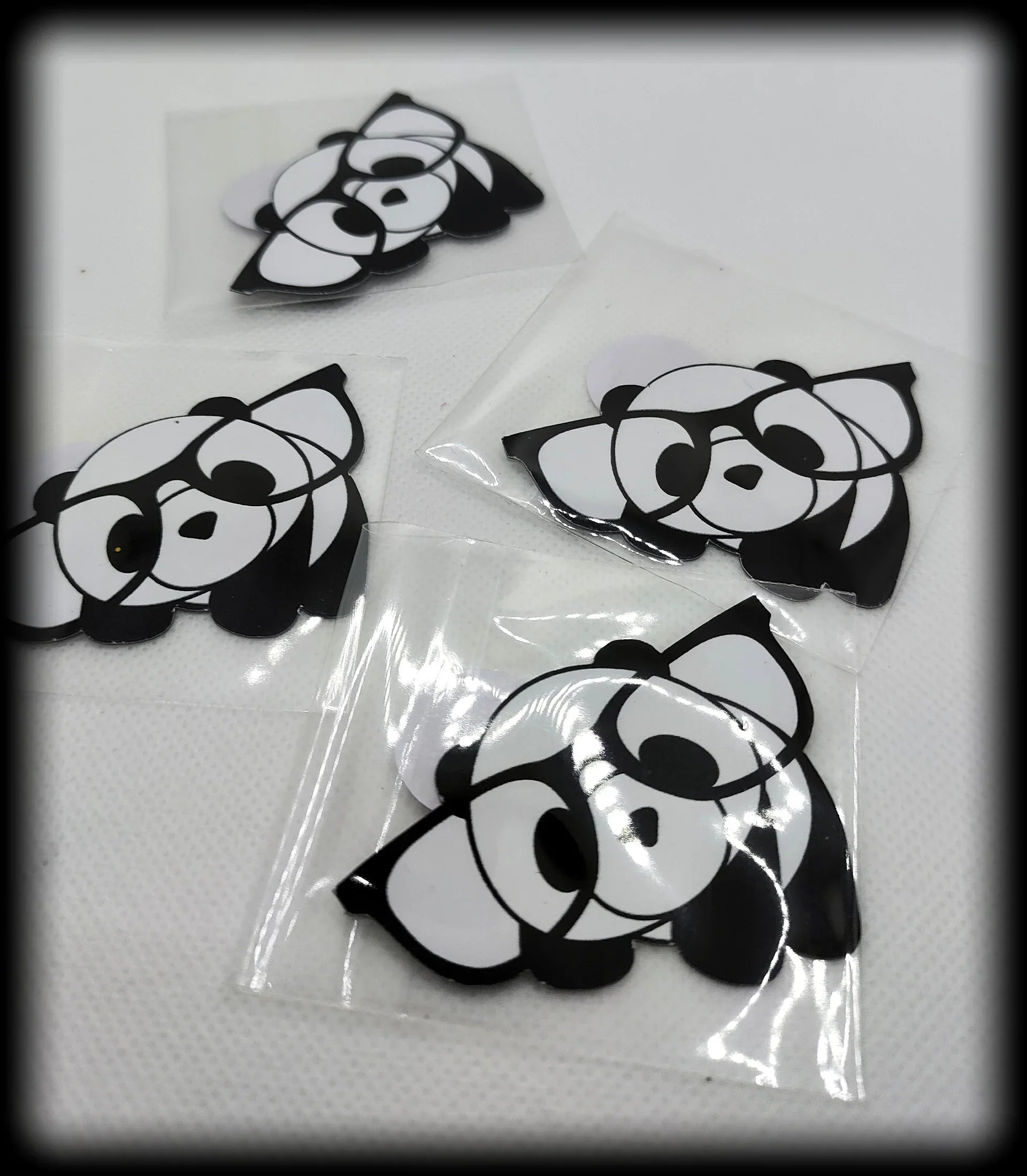 Four black and white panda face stickers on white surface, in clear plastic covers