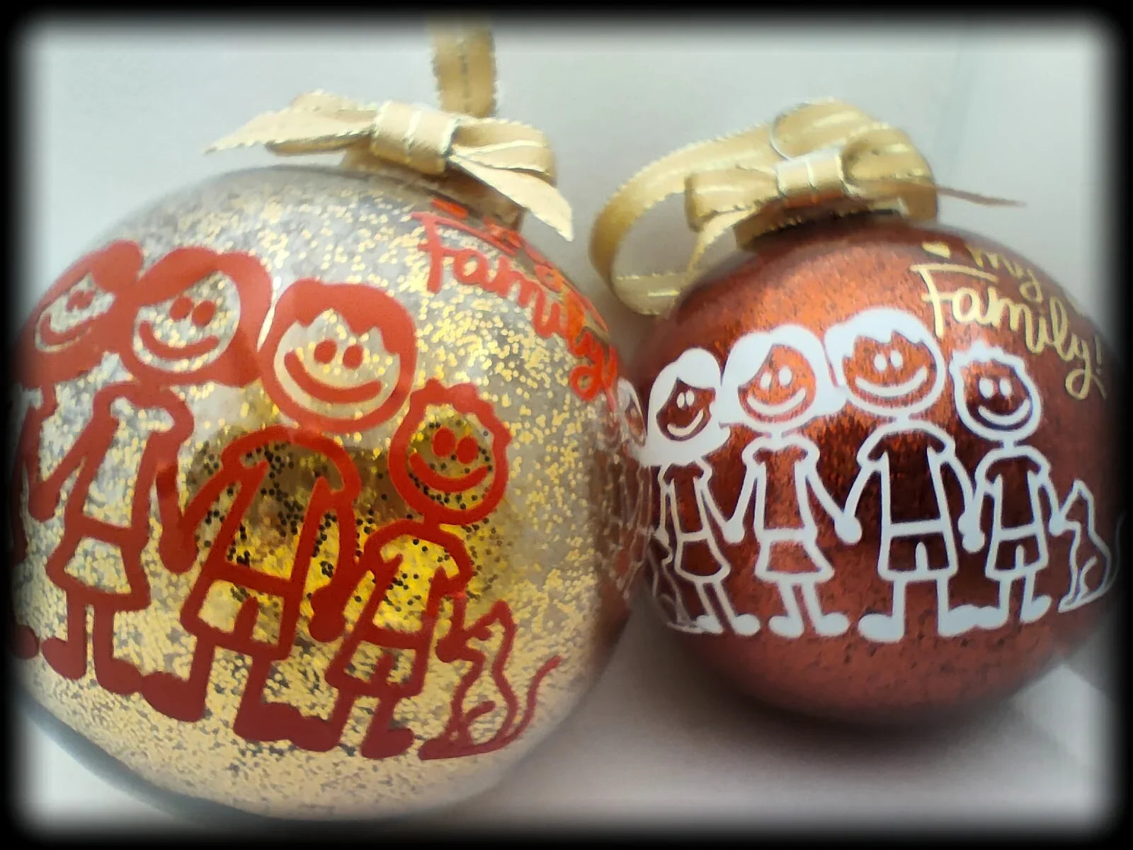 Two glittery Christmas ornaments with stick figure family drawings and gold ribbon bows