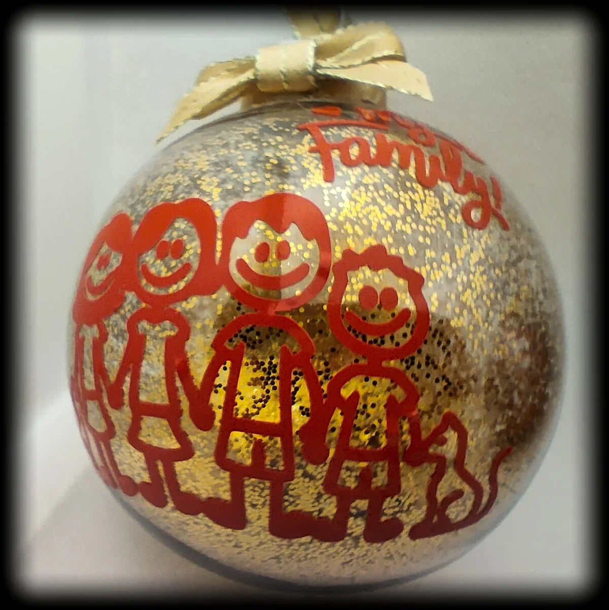 Glittery Christmas bauble with red stick-figure family and cat illustration, gold ribbon
