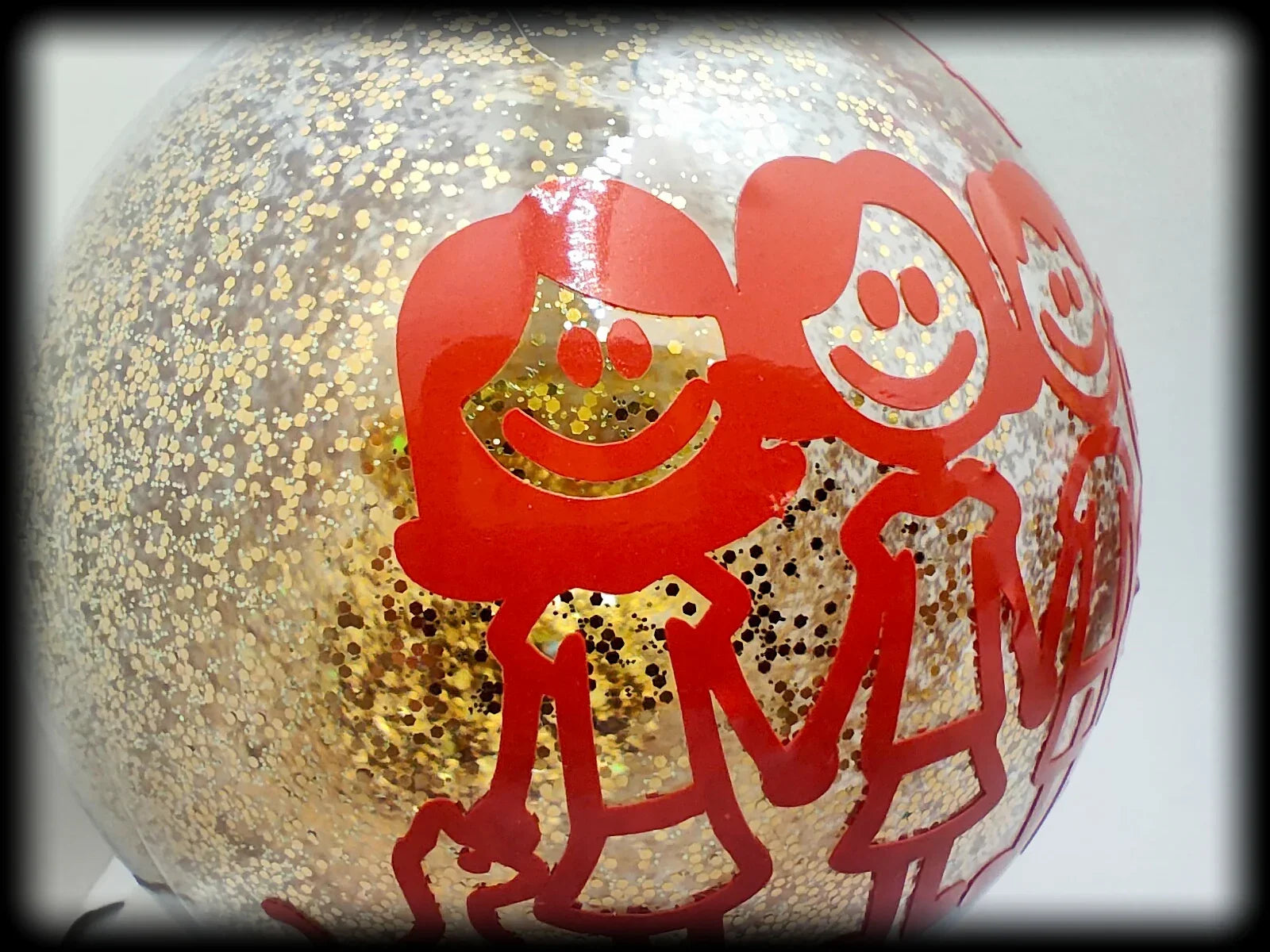 Gold glitter ornament with red stick figure people holding hands, festive holiday decor