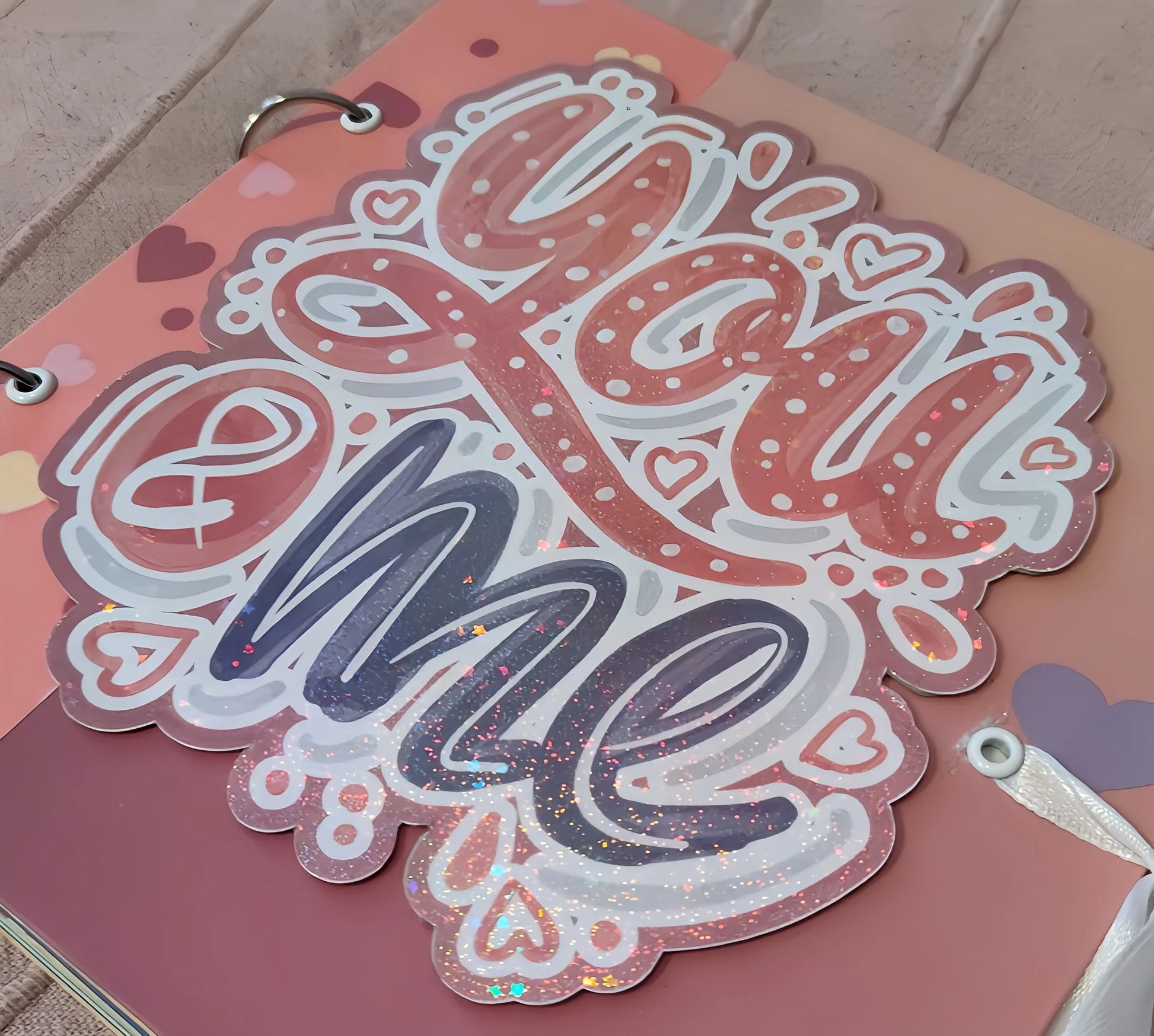 Glittery 'You & Me' sticker on pink heart-themed scrapbook cover
