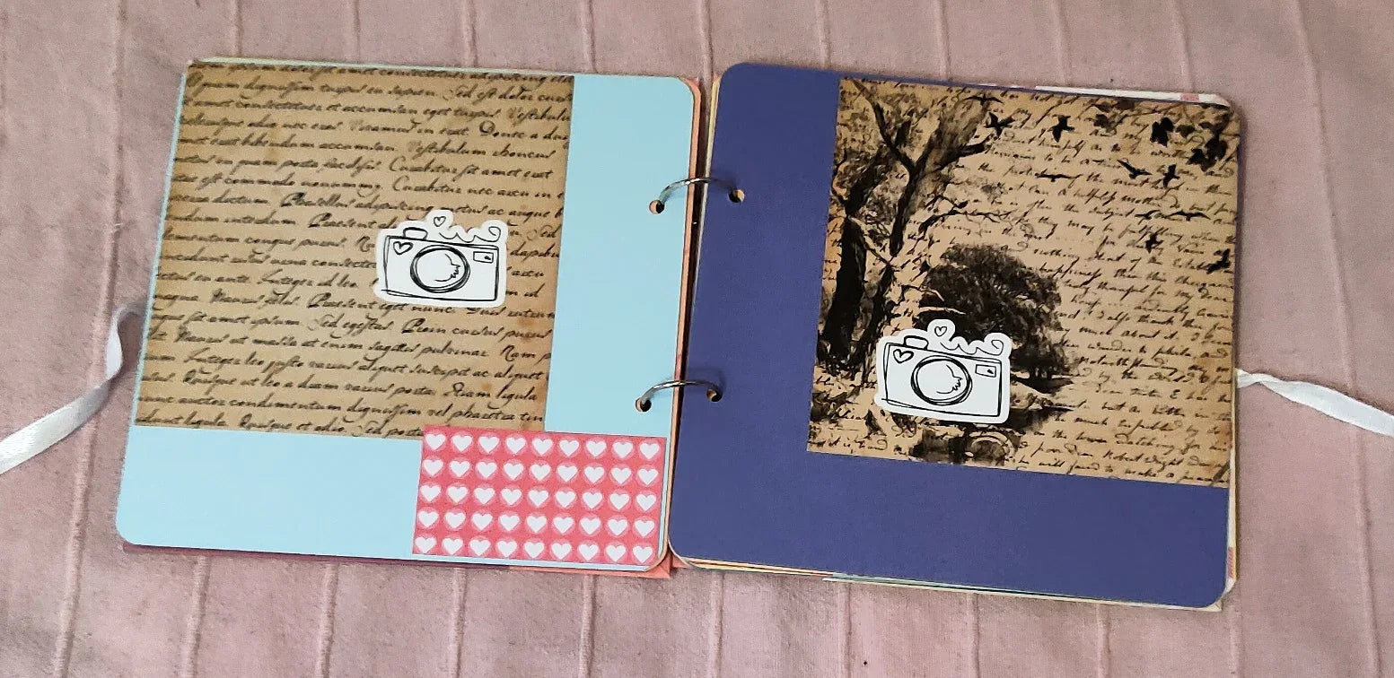 Handmade scrapbook with blue and purple pages, vintage script, heart stickers, and camera icons