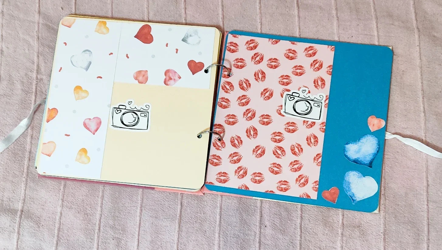 Cute scrapbook pages with heart patterns, camera stickers, and lipstick prints on soft fabric background