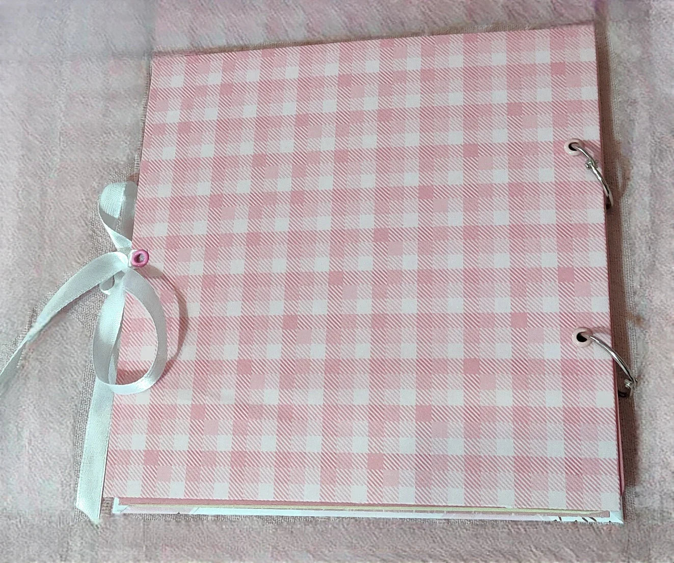 Pink plaid scrapbook with white ribbon and metal rings on a soft pink background