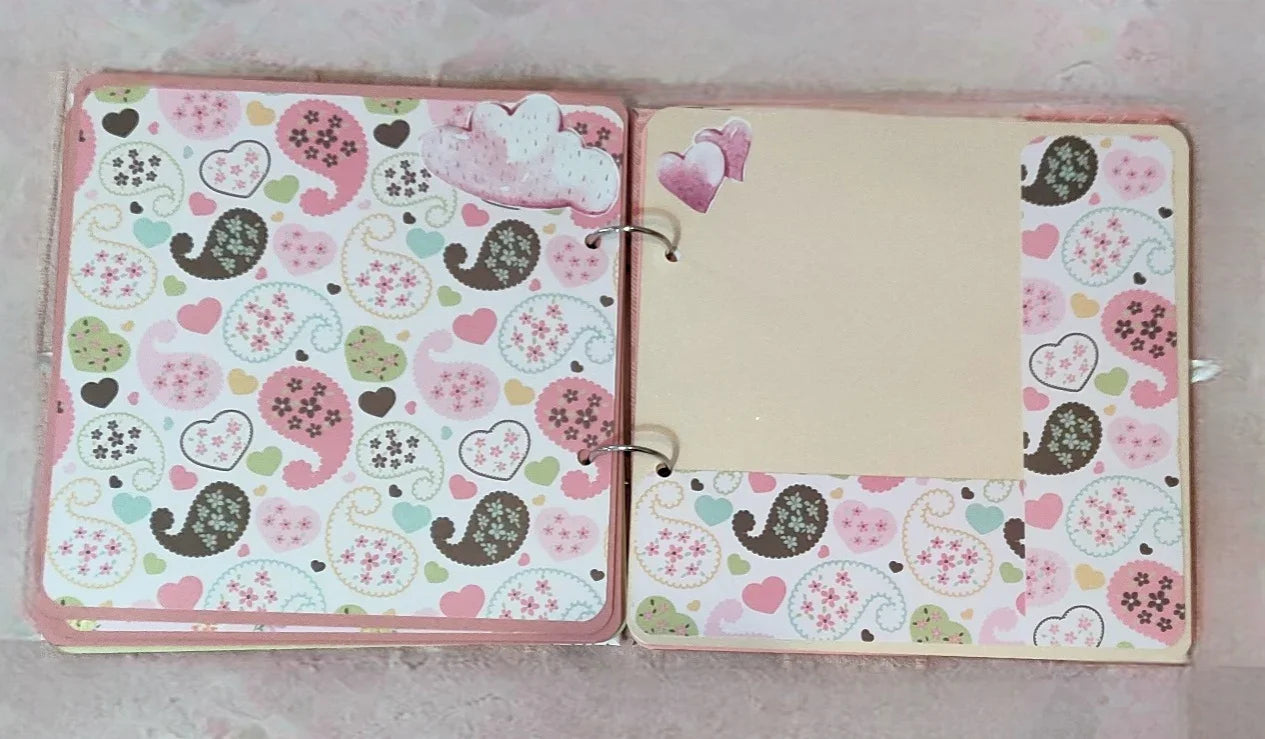 Open scrapbook with pastel paisley and heart patterns, blank photo spot, and cloud stickers