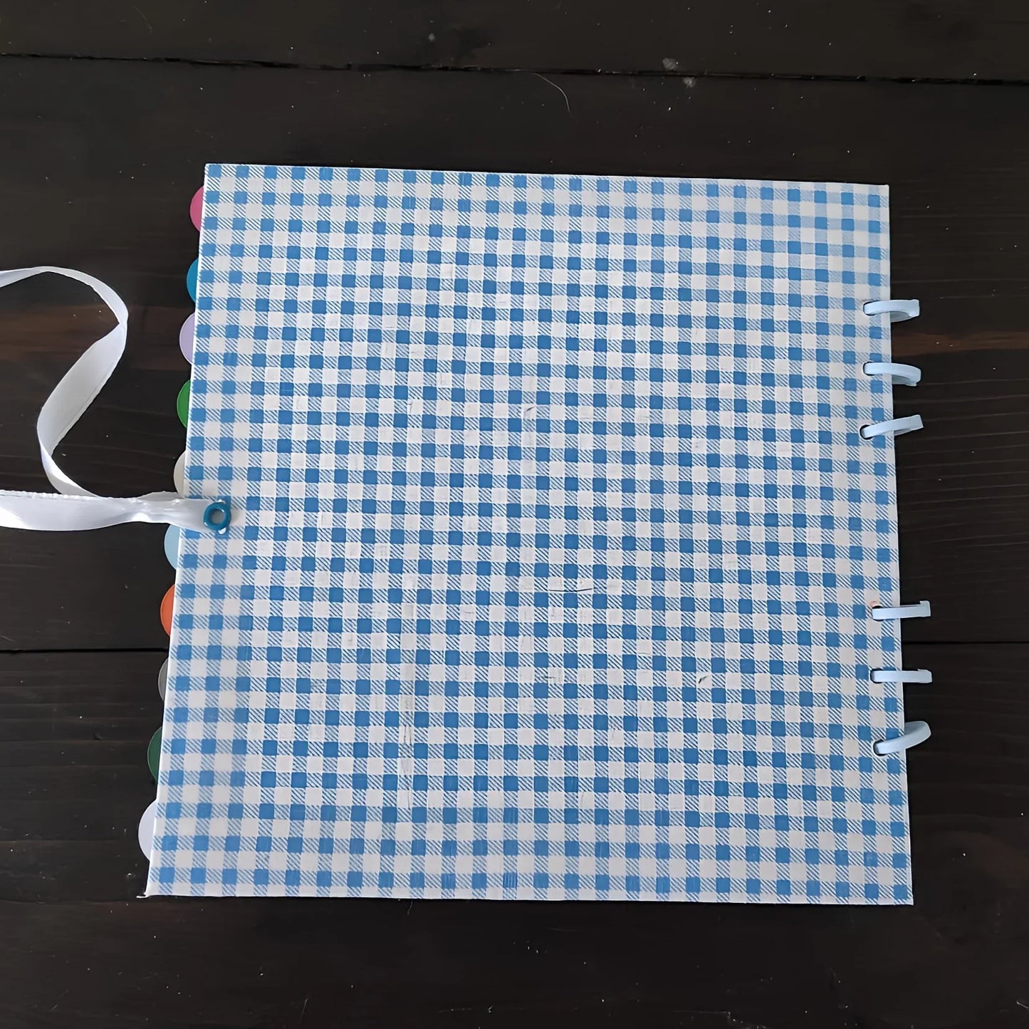 Blue gingham checkered notebook with tabs and ribbon on dark wooden table