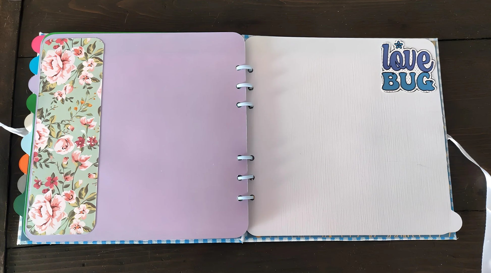 Open scrapbook with floral and pastel pages, 'love bug' sticker on right page