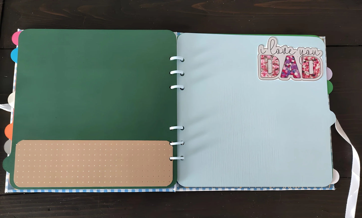 Open scrapbook with green and blue pages, sticker says 'I love you Dad'.