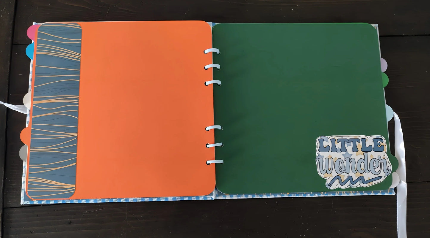 Colorful scrapbook open to orange and green pages, 'Little Wonder' sticker on green page