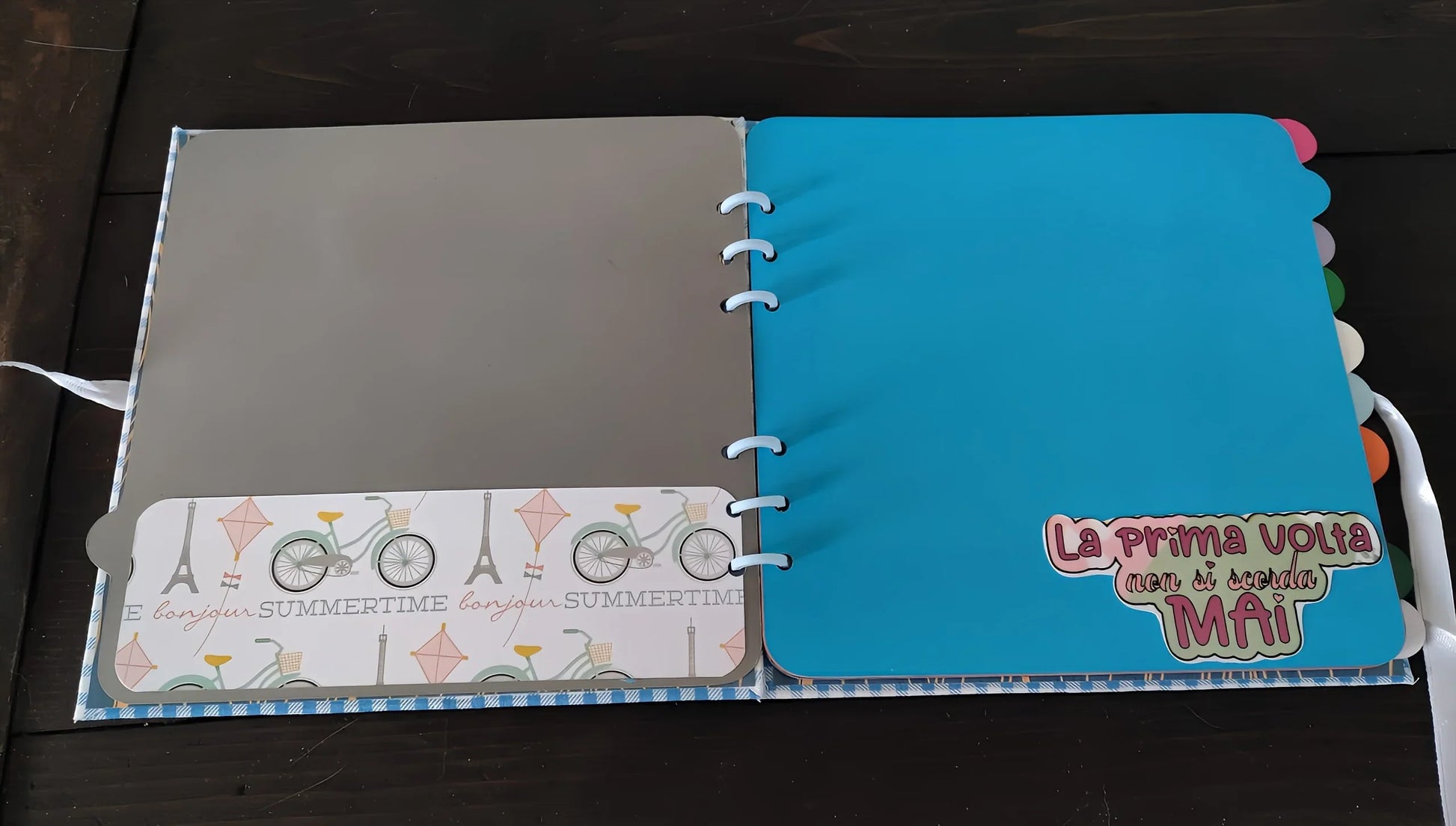 Open scrapbook with grey and blue pages, bicycle pattern, and Italian text sticker