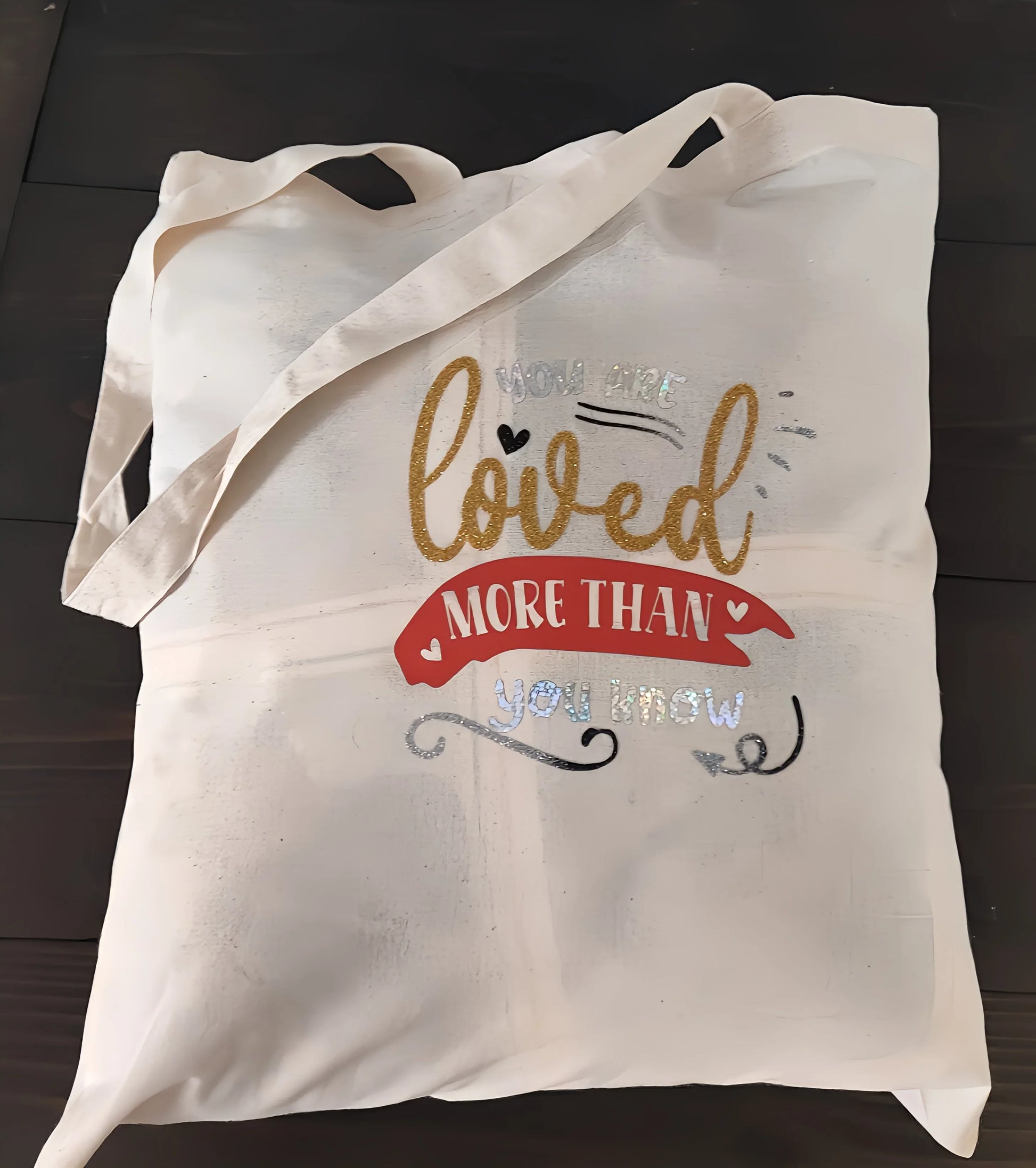 Beige tote bag with 'You are loved more than you know' design on wooden surface