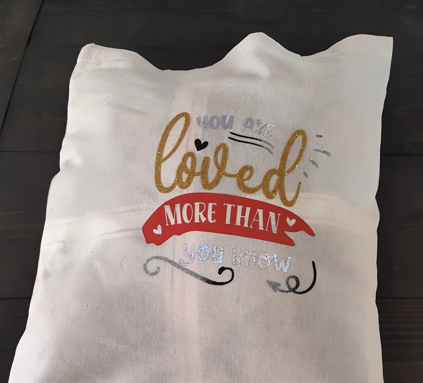 White throw pillow with gold, red, and silver text reading 'You are loved more than you know'