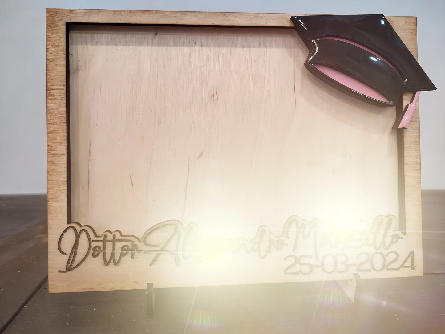 Wooden graduation picture frame with black cap and engraved date 25-03-2024 on display table