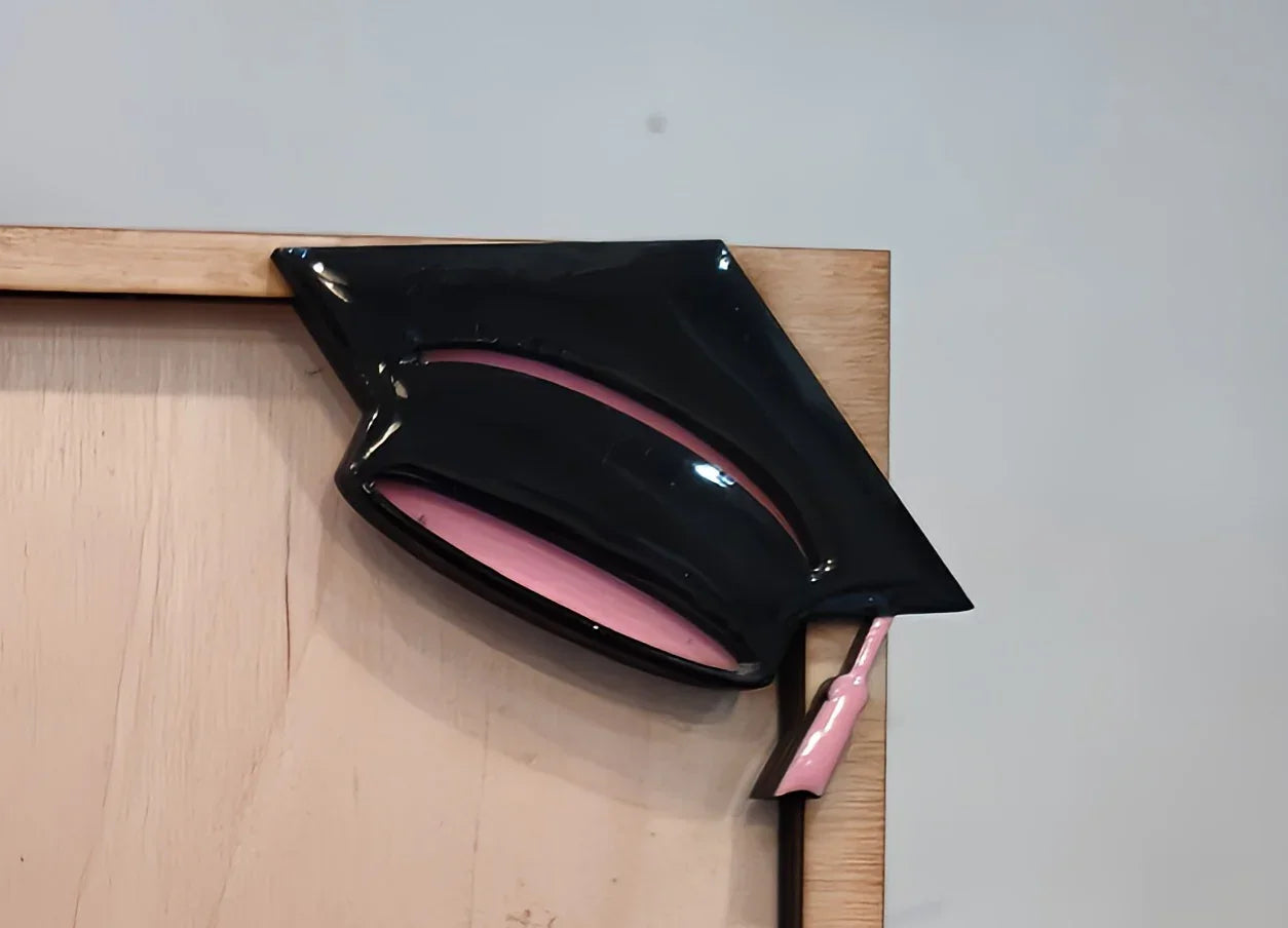 Black and pink ceramic graduation cap decoration on wooden frame
