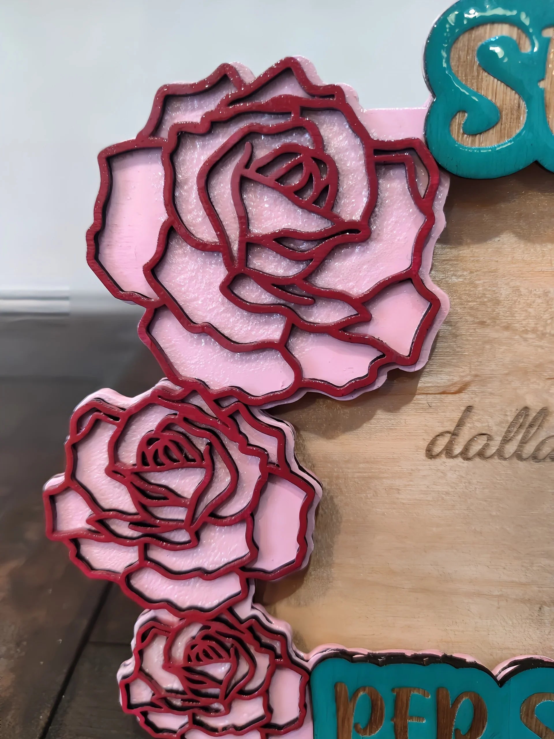Layered pink and red rose decorations on a wooden sign with engraved letters