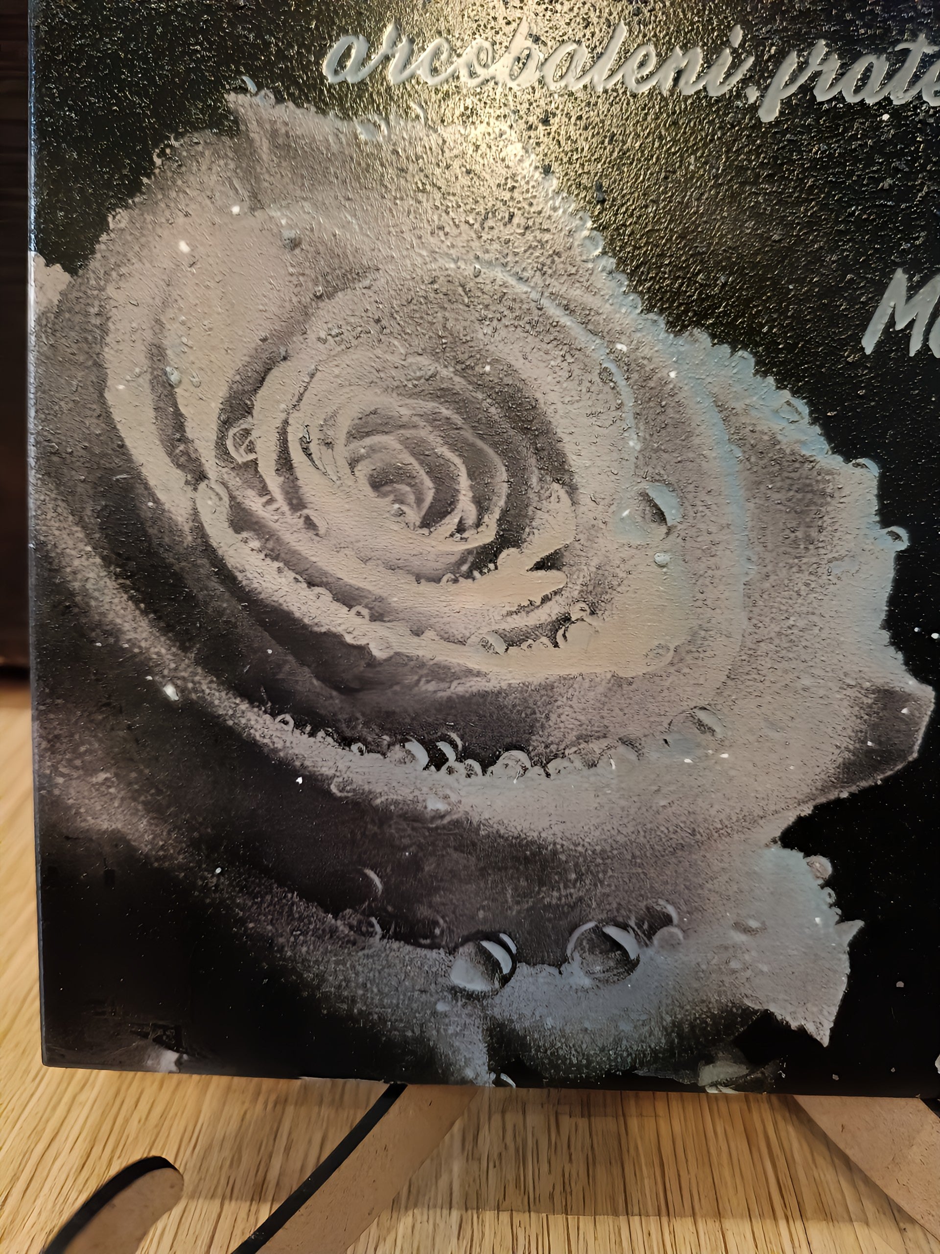 Black and white rose with water droplets on a textured canvas, displayed on a wooden stand