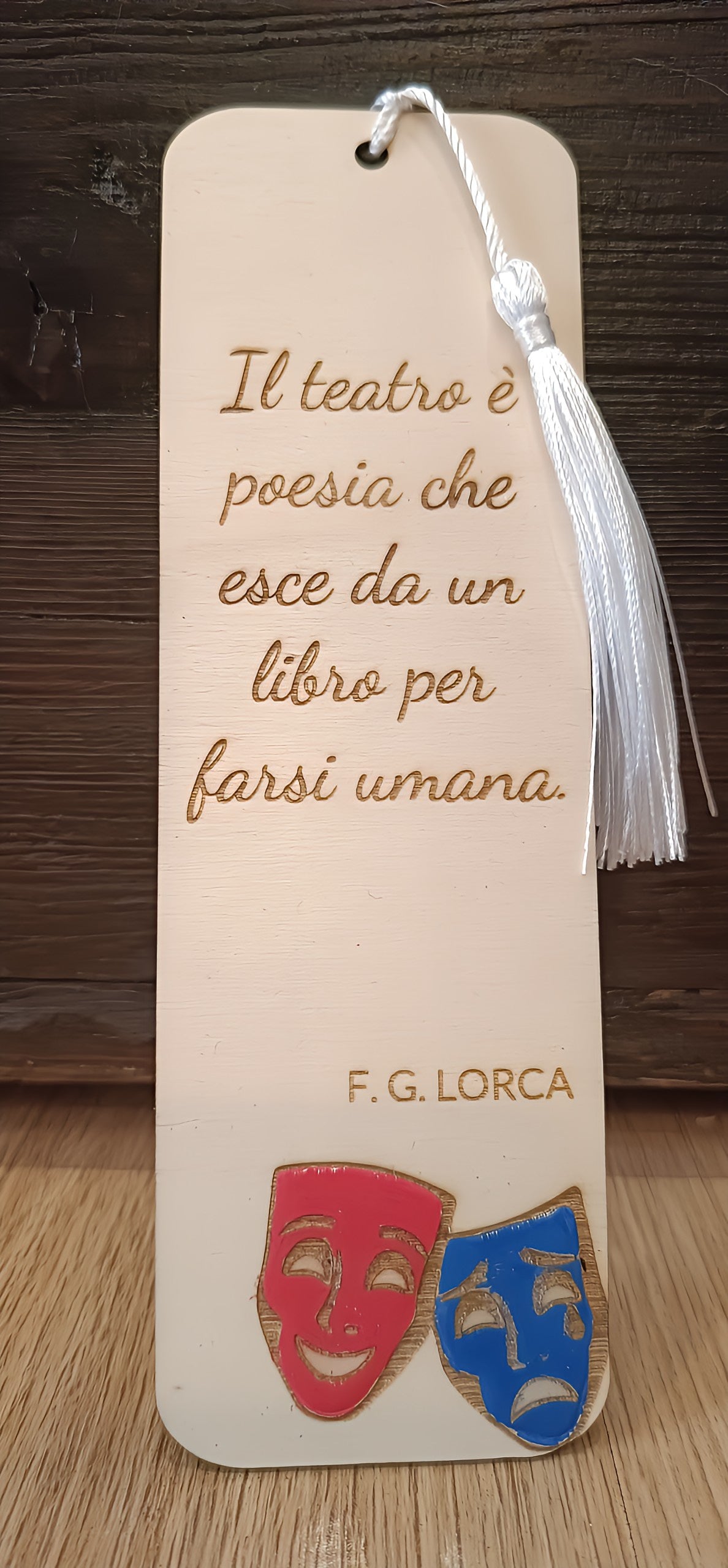 Wooden theater bookmark with Italian quote, drama masks, and white tassel on wood background