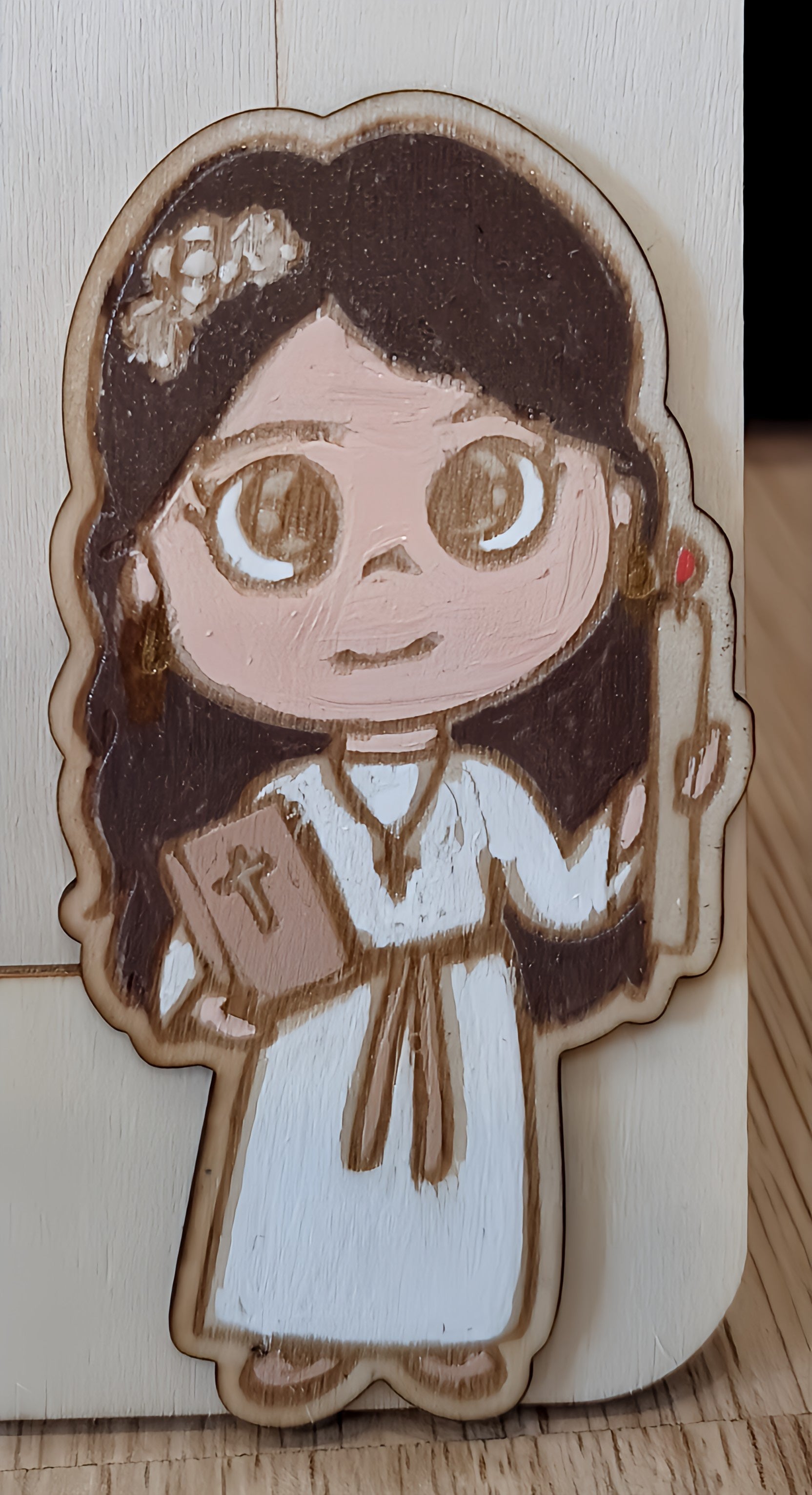 Hand-painted wooden figure of a girl in white with candle and Bible on wood background