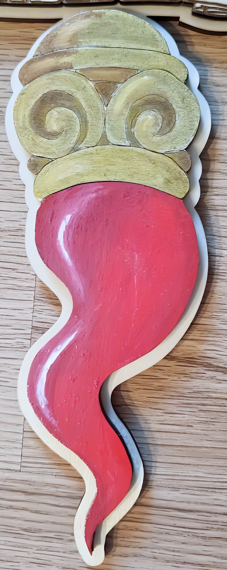 Wooden red Italian cornicello charm with gold swirls on light wood background