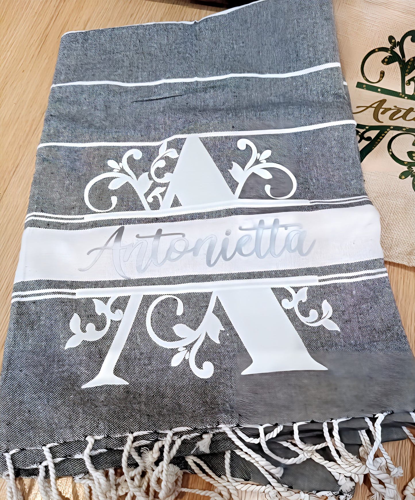 Personalized gray towel with white Antonietta name and monogram design on wood surface