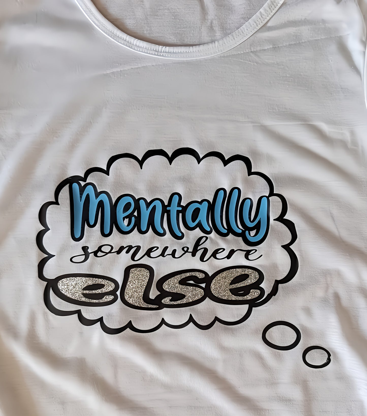 White t-shirt with text bubble graphic saying 'Mentally somewhere else' in glitter and blue print.