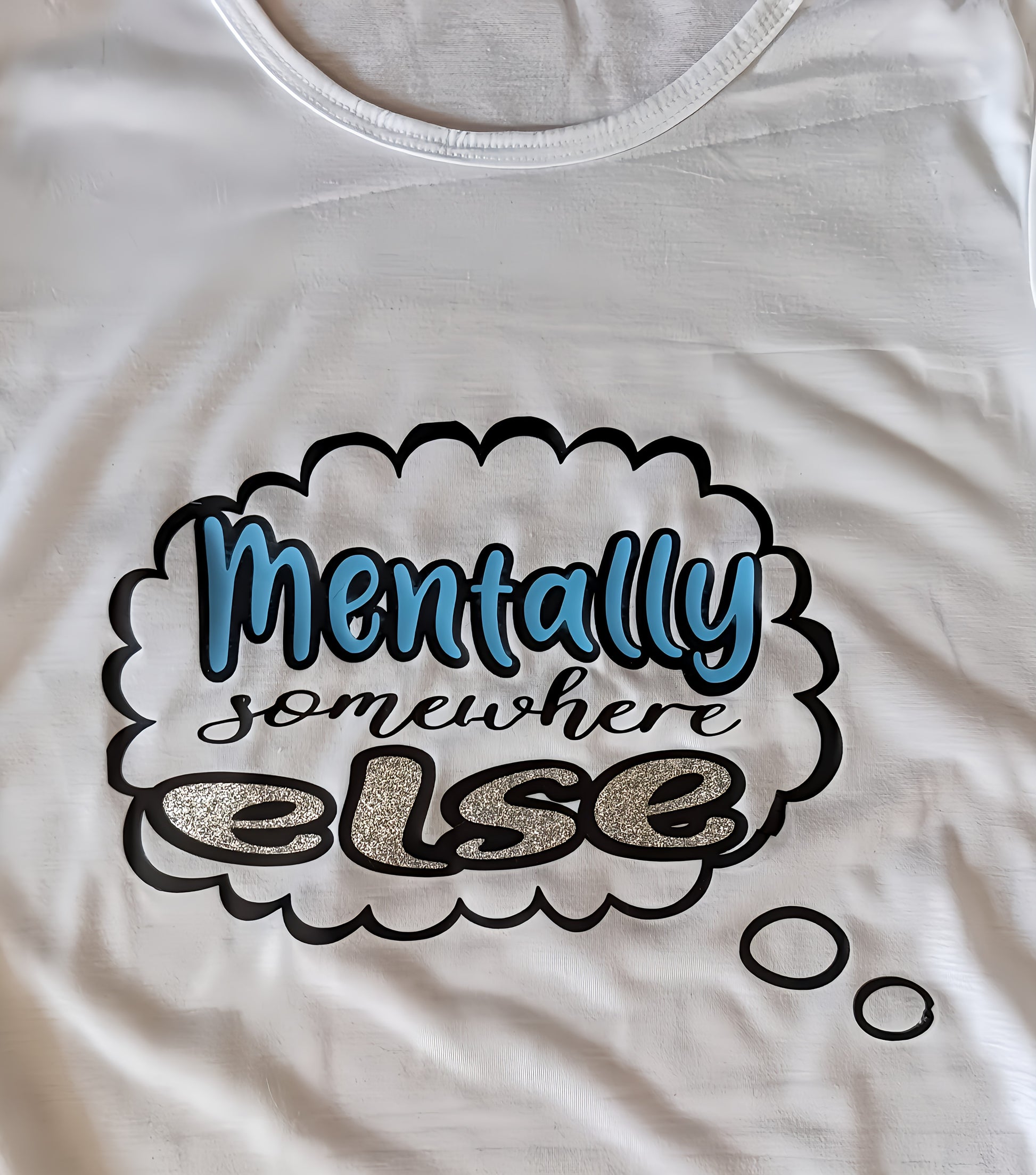 White t-shirt with text bubble graphic saying 'Mentally somewhere else' in glitter and blue print.