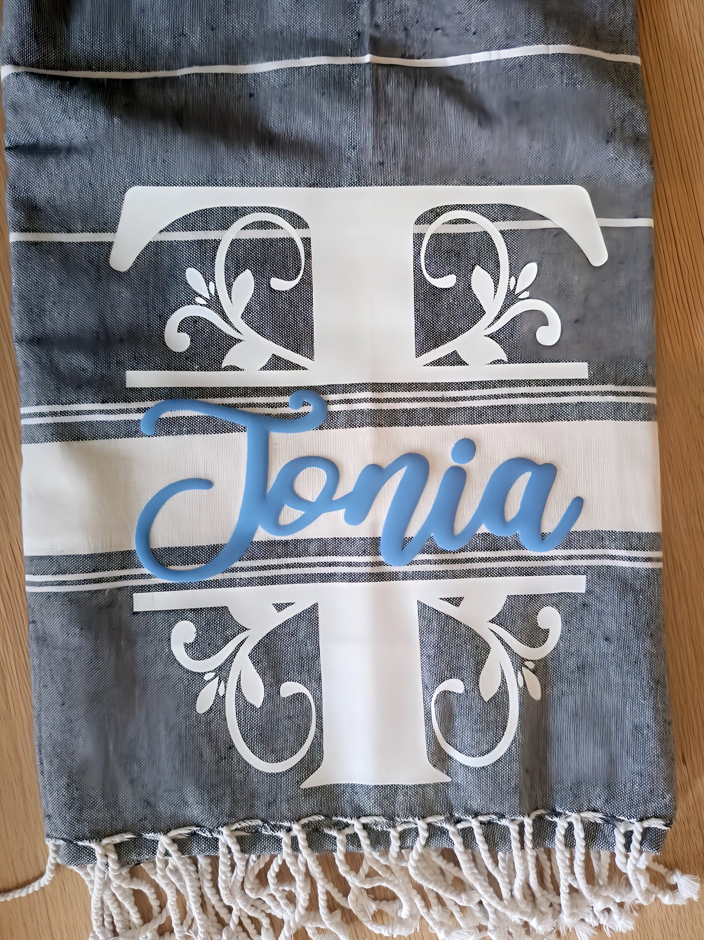 Personalized gray towel with white T monogram, blue Jonia name, and tasseled fringe.