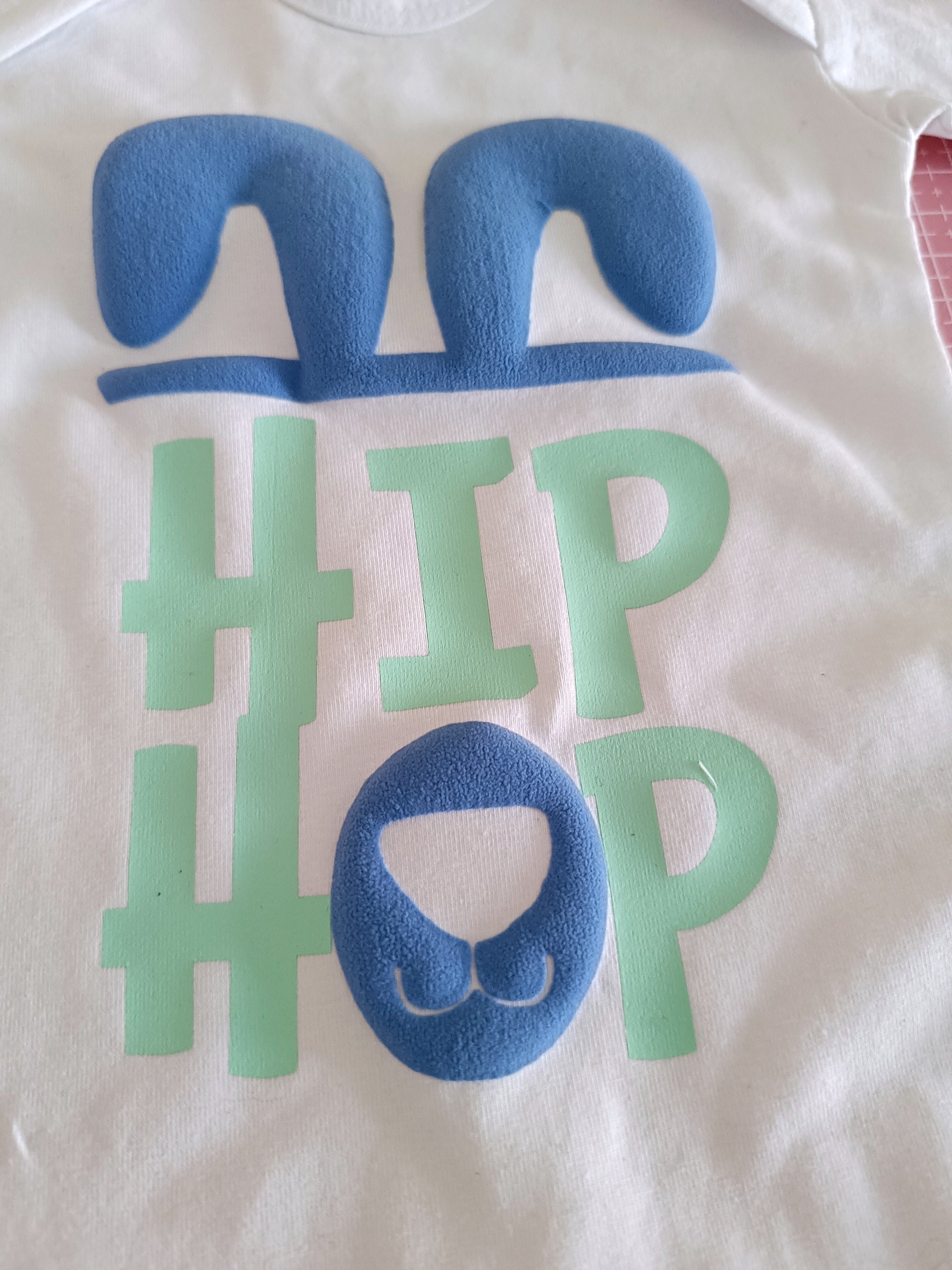White baby onesie with blue bunny ears, snout and green hashtag HIP HOP text design