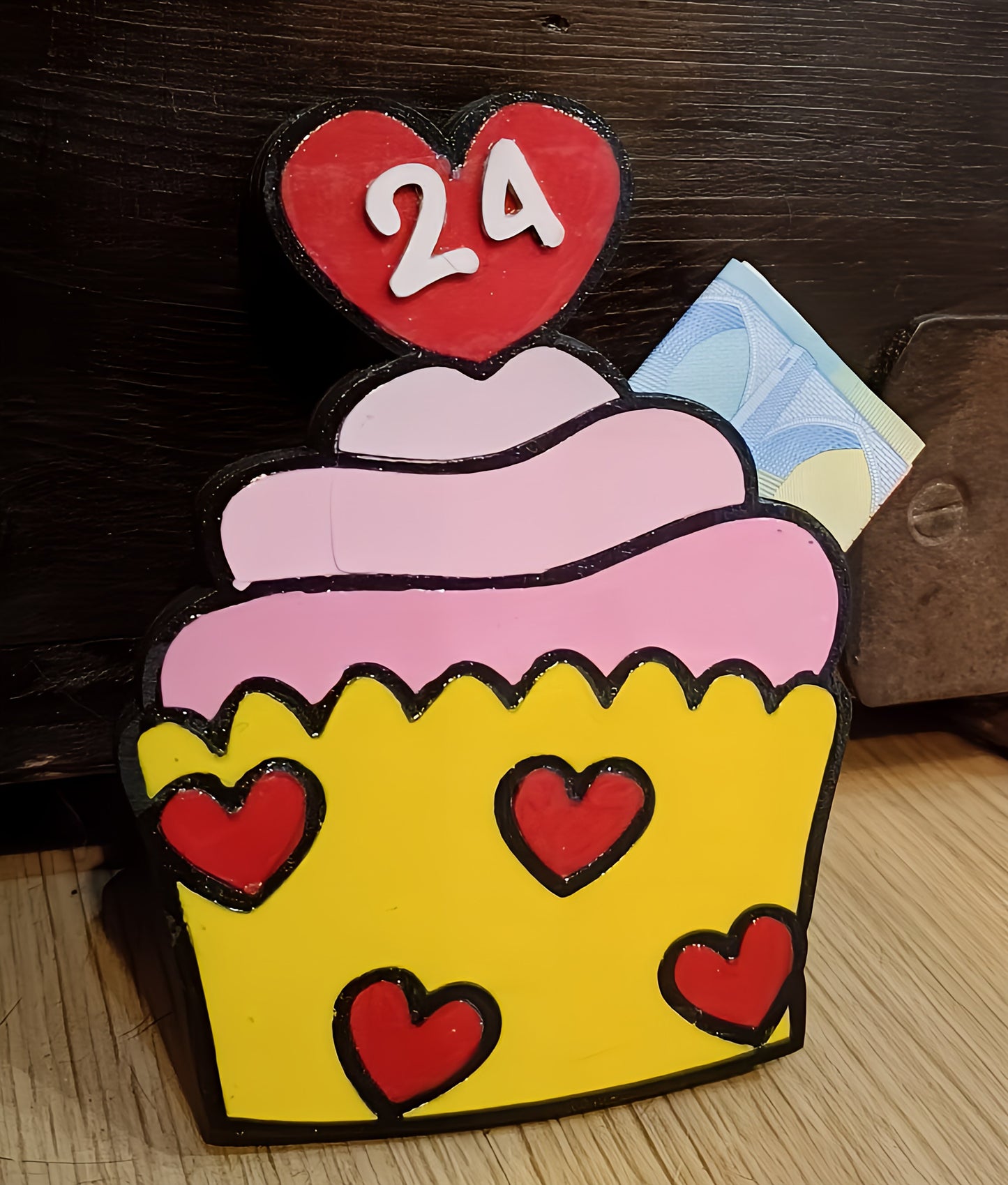 Colorful cupcake-shaped box with red hearts, number 24, and euro note on wood background