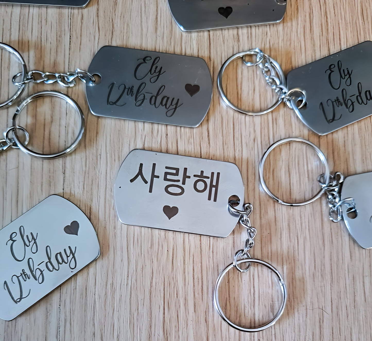 Engraved metal keychains with 'Ely 12th b-day' and Korean '사랑해' on wood table