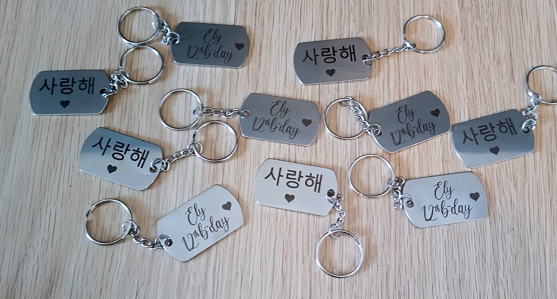 Metal keychains on wood table engraved with 'Ely 12th b-day' and '사랑해' with heart