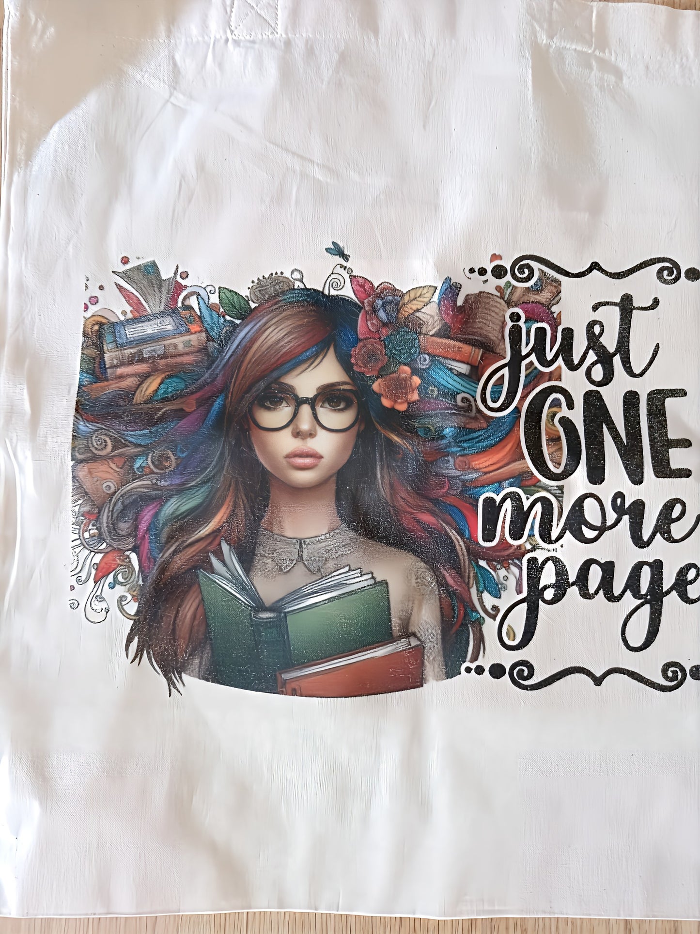 Tote bag with illustrated woman holding books, colorful hair, 'just one more page' text
