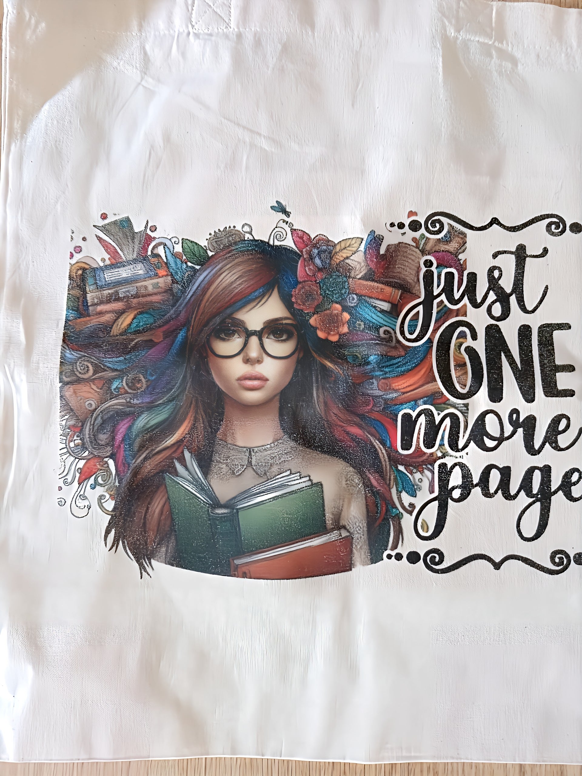 Tote bag with illustrated woman holding books, colorful hair, 'just one more page' text
