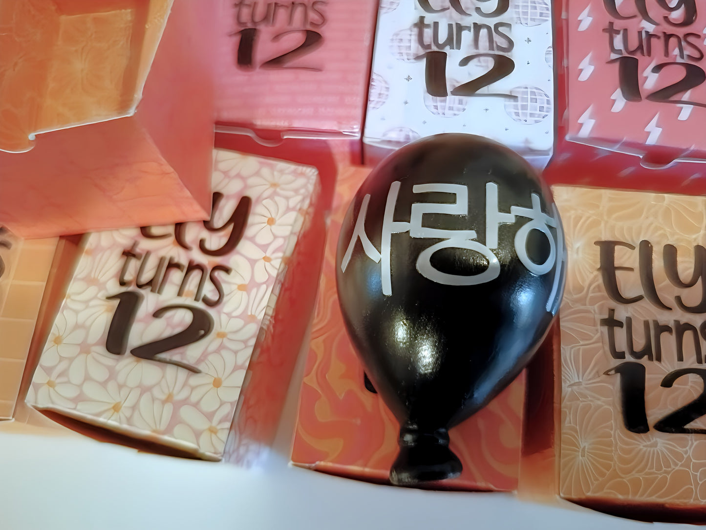 Black balloon with Korean text among colorful 'Ely turns 12' party favor boxes