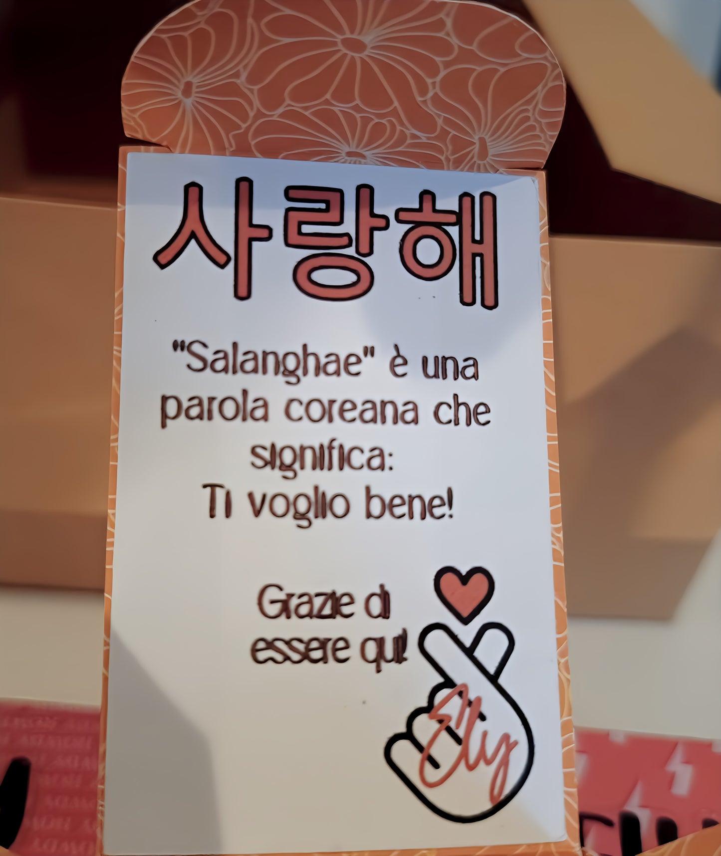 Korean word 'Saranghae' sign with Italian translation, floral border, hand heart illustration