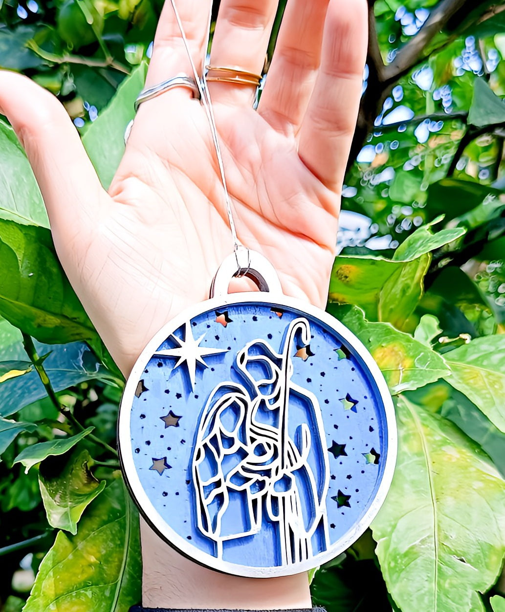 Hand holding nativity scene Christmas ornament with blue starry background outdoors