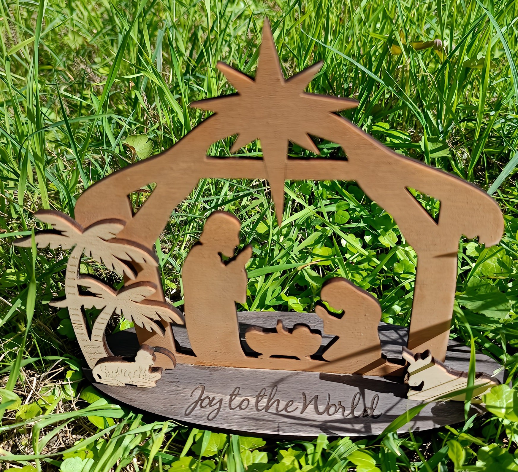 Wooden nativity scene with 'Joy to the World' text on green grass outdoors