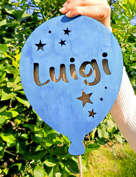 Blue balloon-shaped wooden sign with cut-out stars and 'Luigi' held outdoors by hand