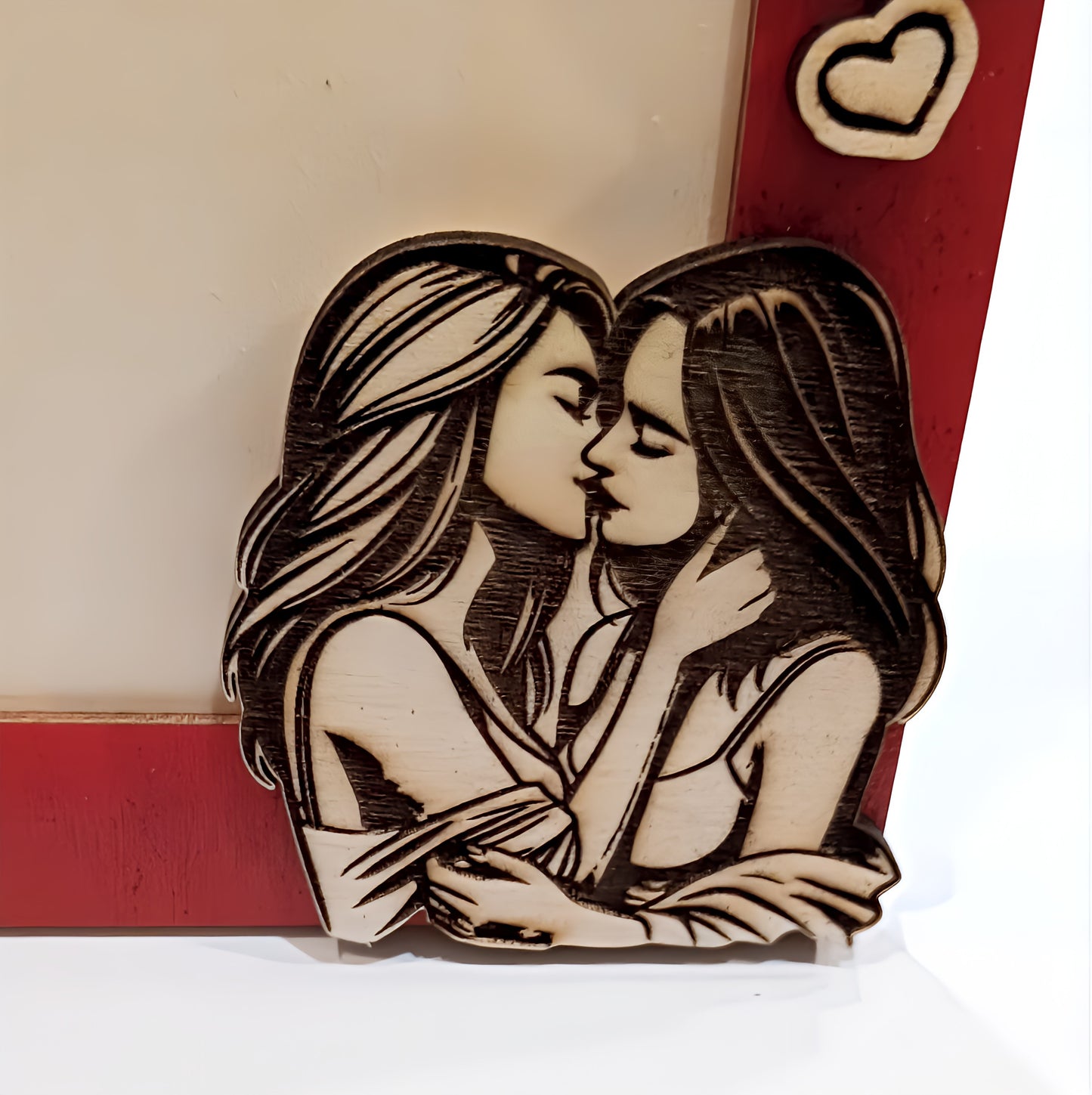 Wooden engraving of two women kissing on a red photo frame with heart detail