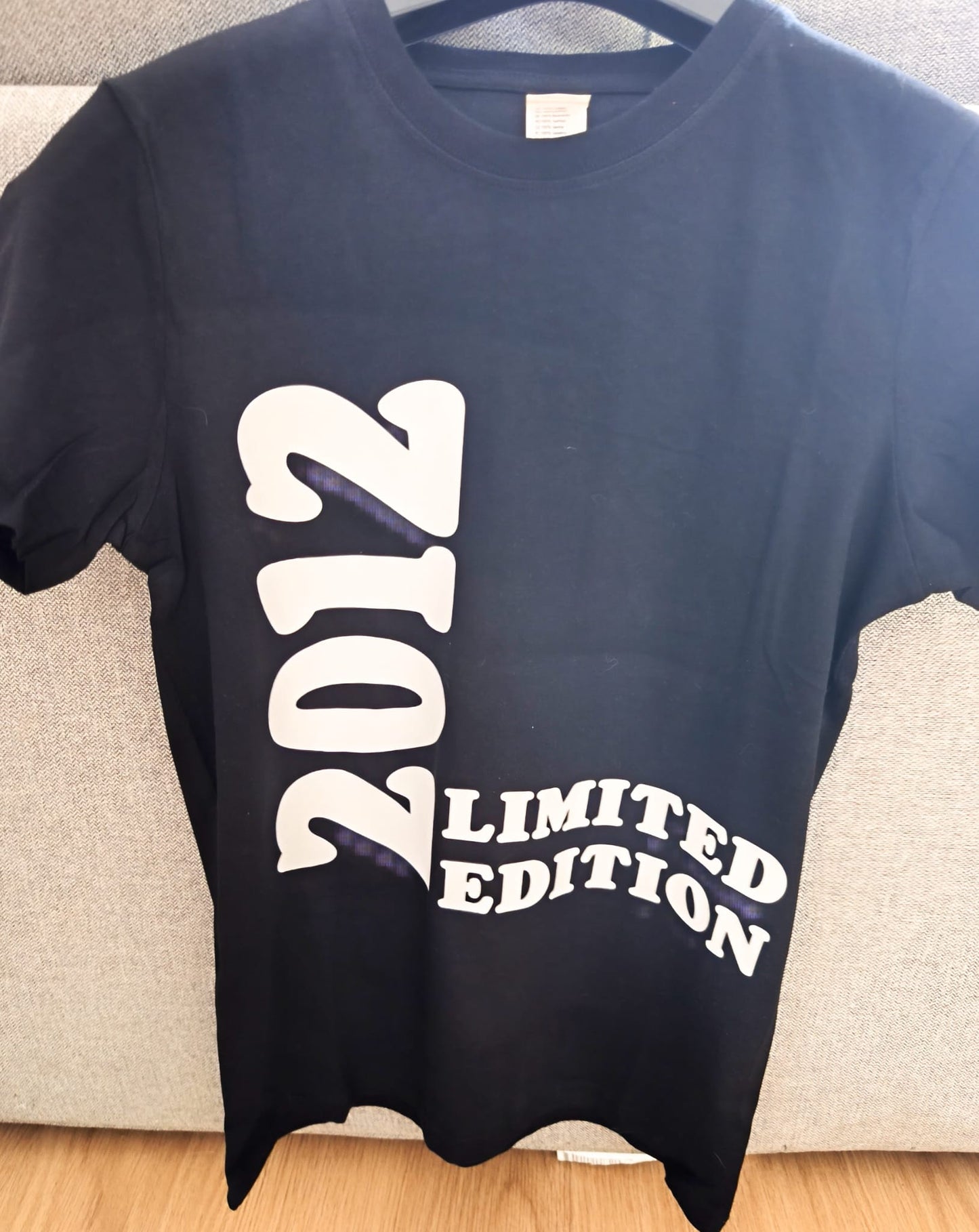 Black t-shirt with bold white 2012 Limited Edition print, hanging on a hanger