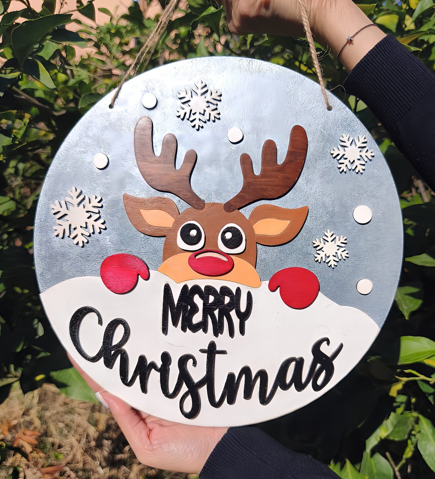 Hand holding round Merry Christmas sign with reindeer, snowflakes, and festive design