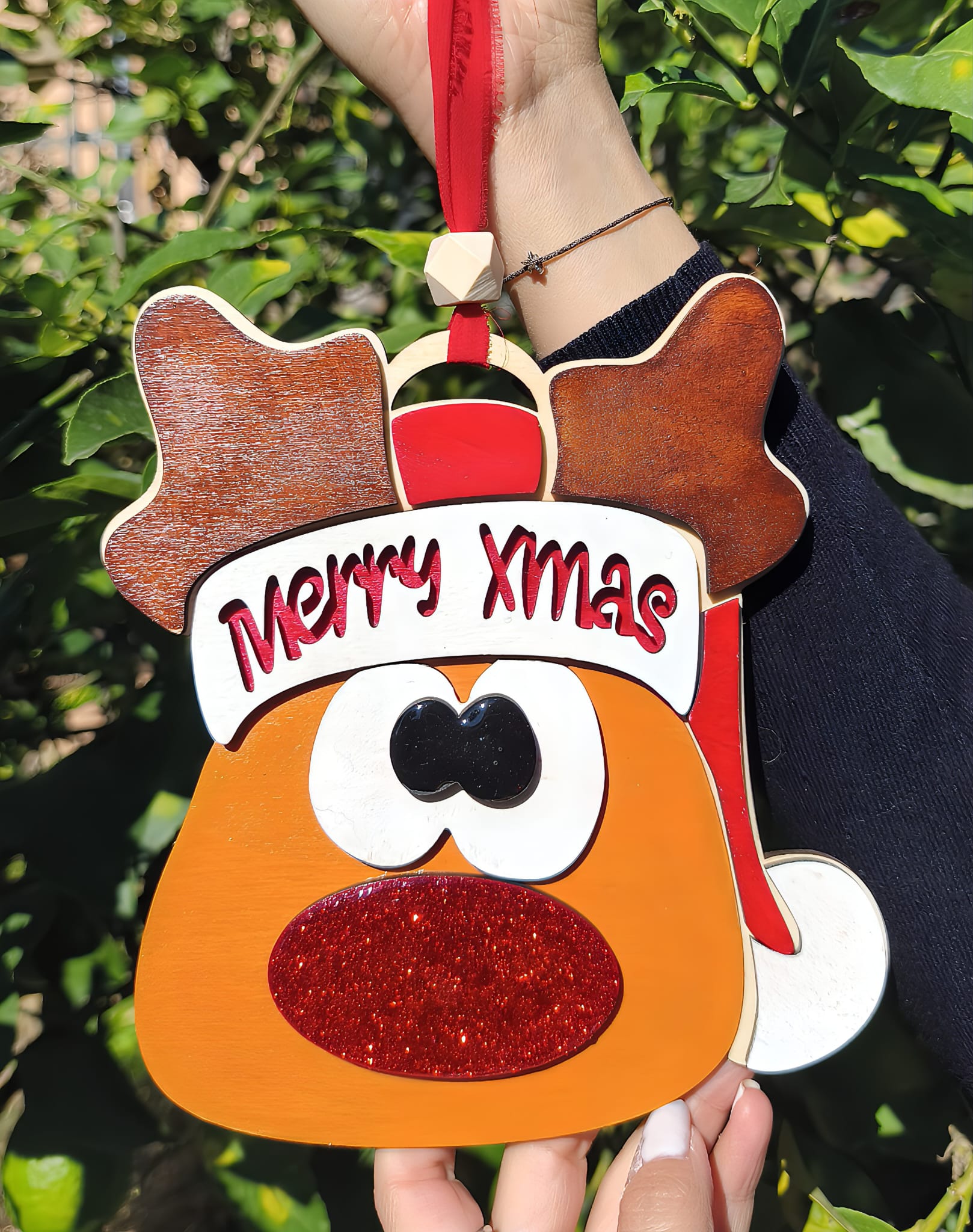 Hand holding reindeer Merry Xmas ornament with red glitter nose outdoors, Christmas decoration