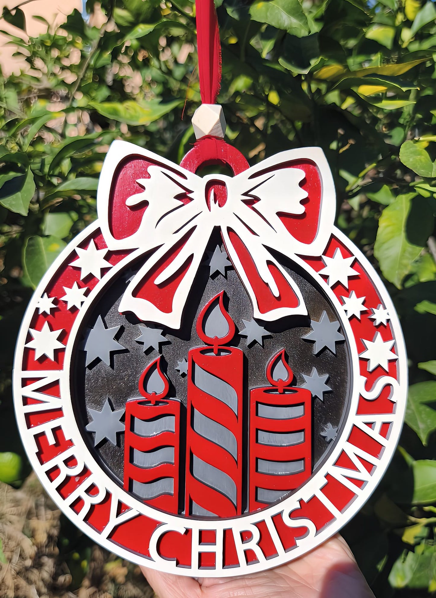 Red and white Merry Christmas ornament with candles and bow hanging outdoors