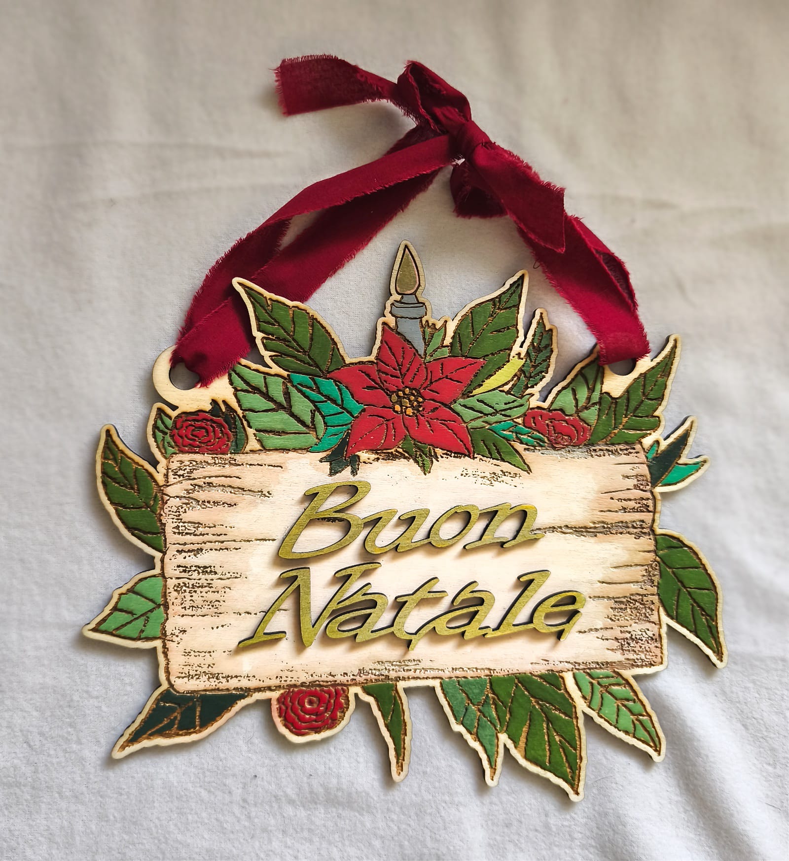 Wooden Buon Natale Christmas sign with poinsettias, green leaves, and red ribbon on white cloth
