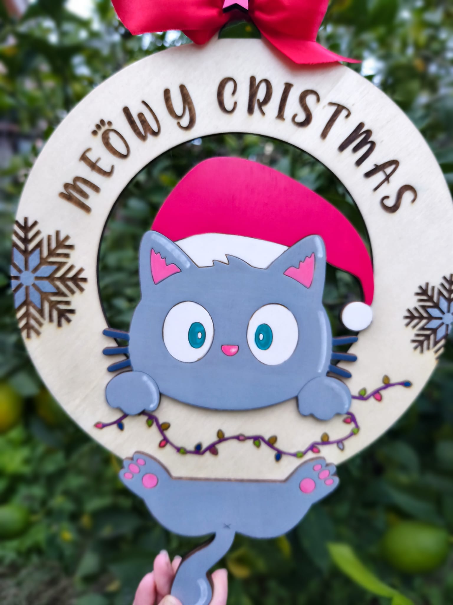 Cute cat Christmas wreath with 'Meowy Christmas' text, red bow, and festive lights outdoors
