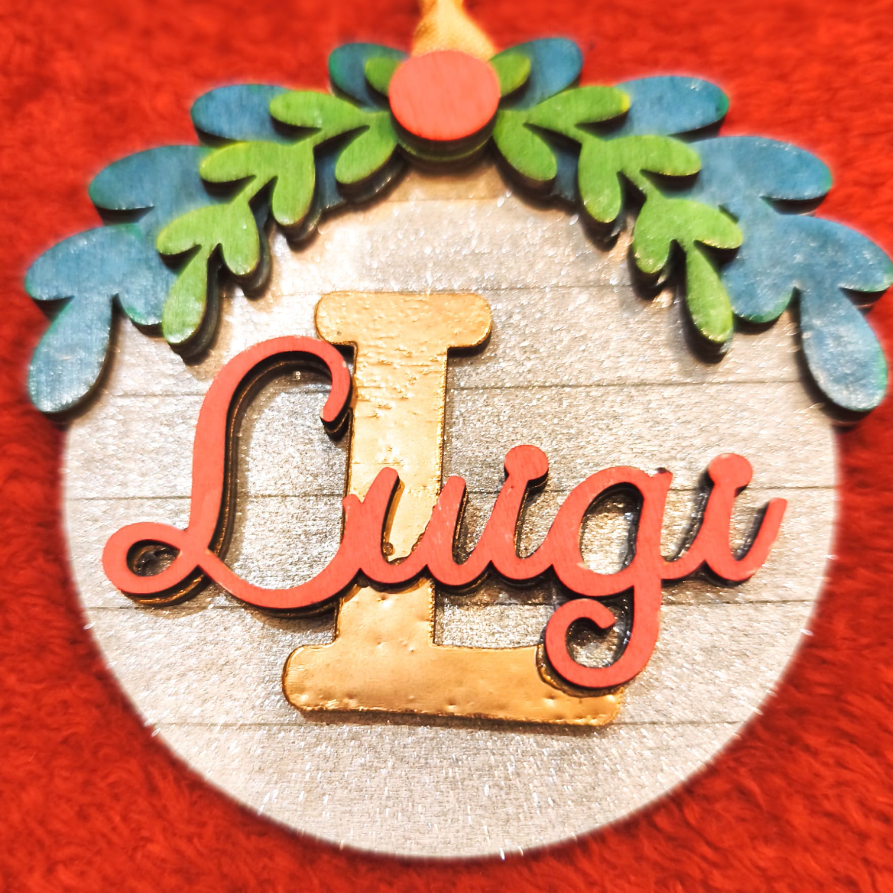 Dettaglio ravvicinato pallina Natale personalizzata legno con scritta Luigi corsivo corallo e iniziale dorata